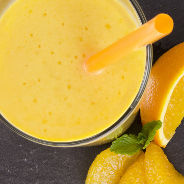 Apfel-Bananen-Orangen-Smoothie im Glas mit Strohhalm und angeschnittenem Obst daneben.