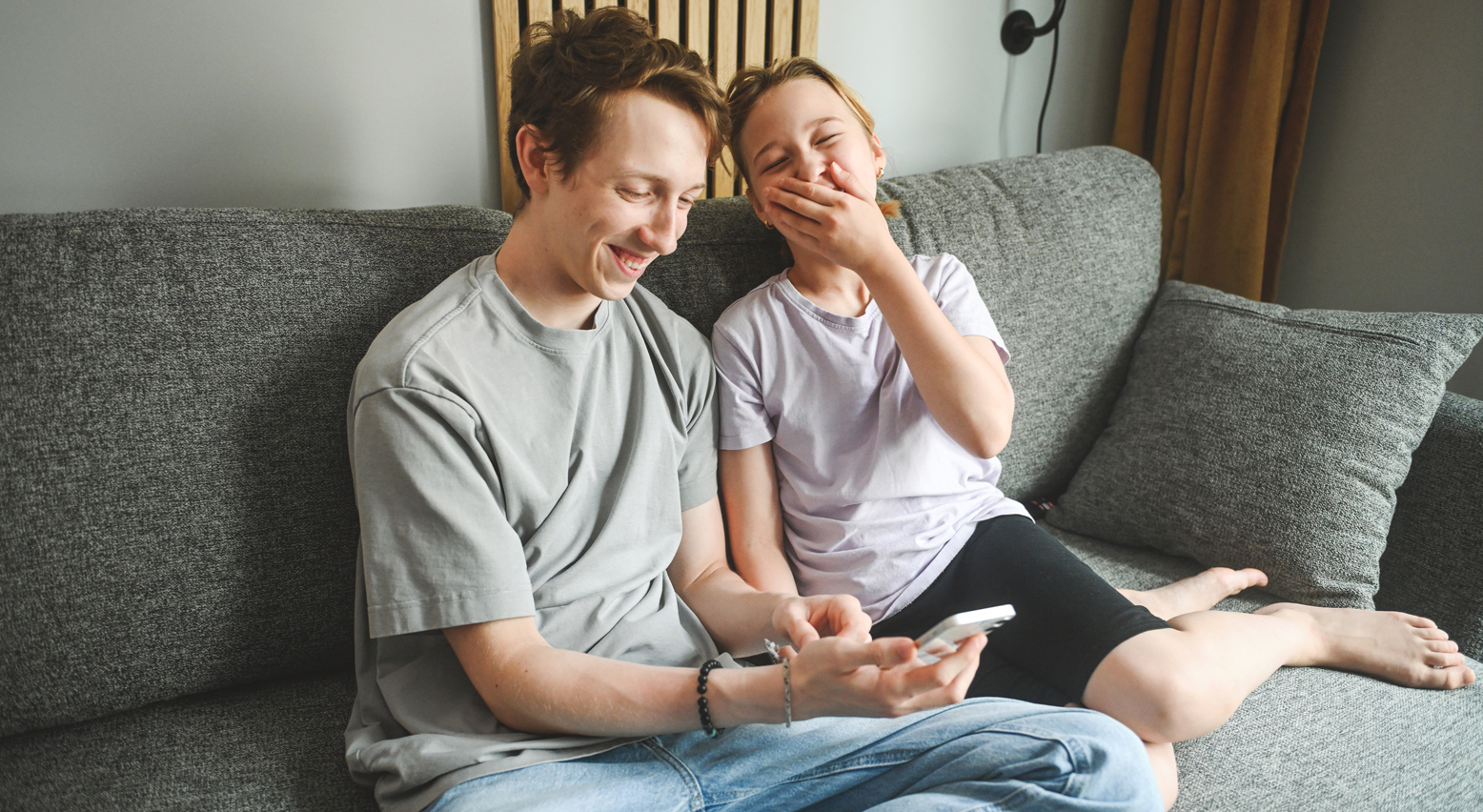 Teenager sitzen mit Handy nebeneinander und lachen